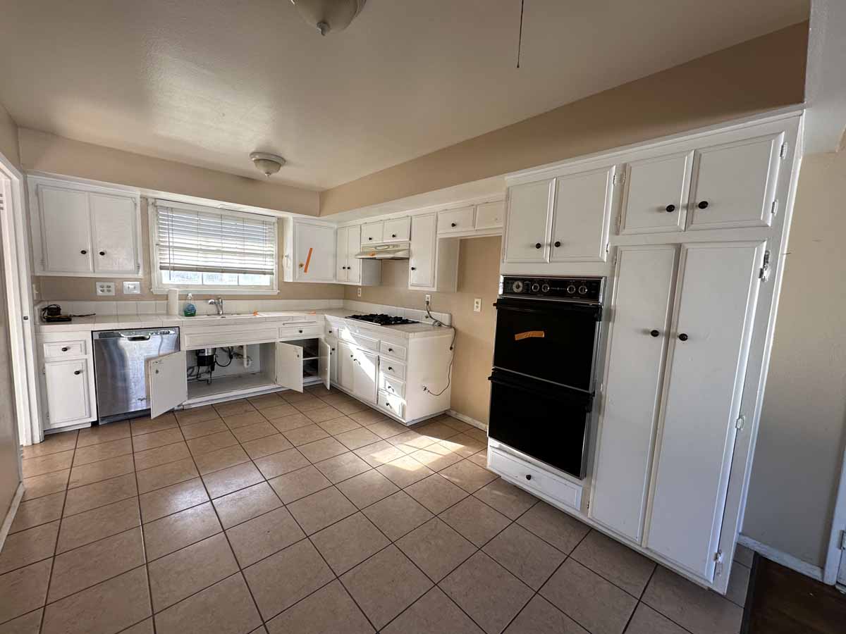 Outdated kitchen with tile flooring, old white cabinets and a black oven.