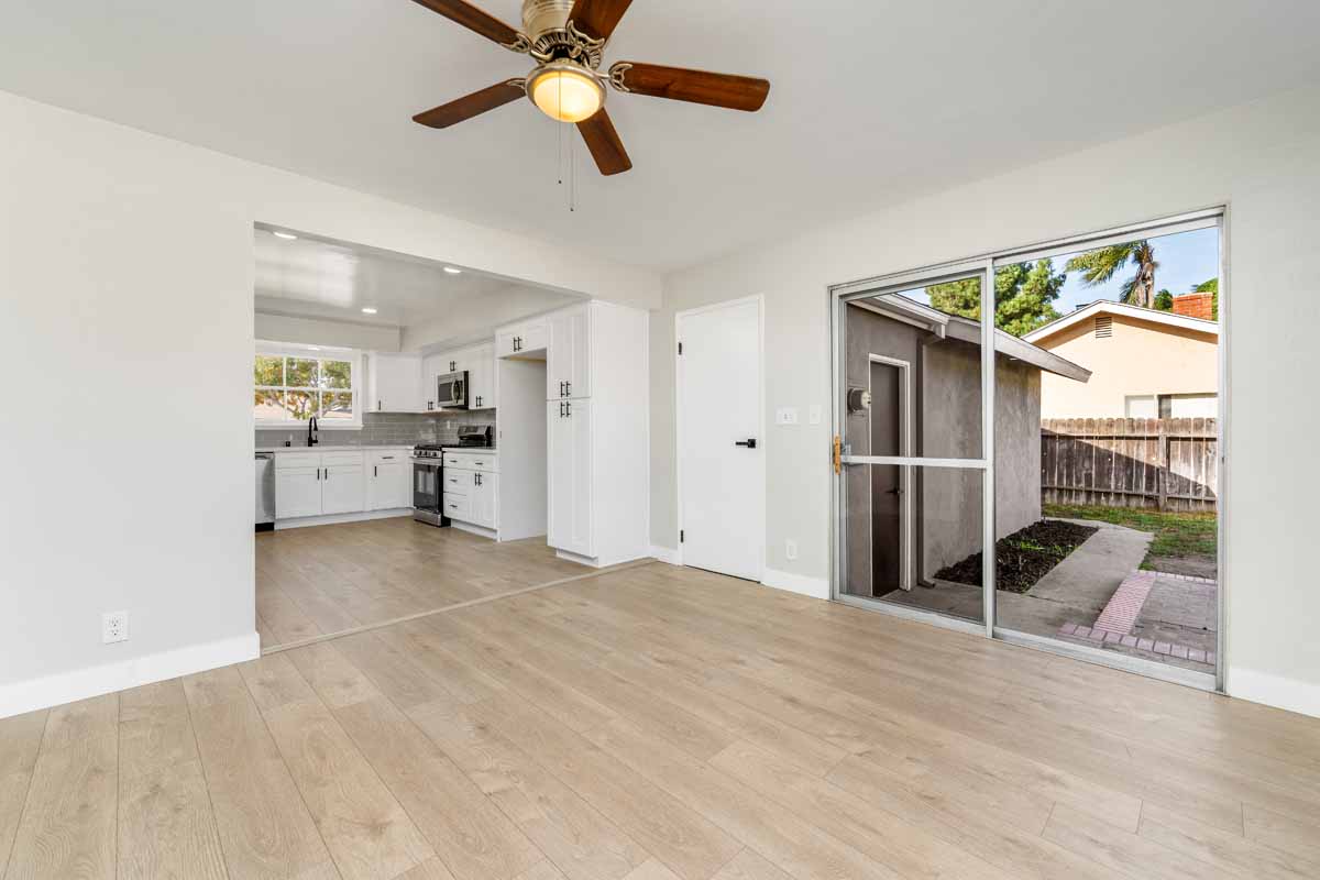 Neutral colored floors and walls of a dining space off the kitchen showing a ceiling fan and sliding glass doors leading to the backyard.