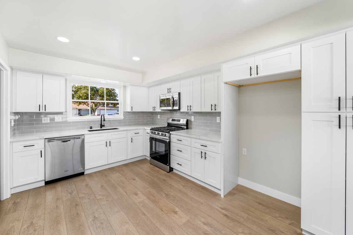 An updated kitchen with white cabinets, light stone counter tops and stainless appliances.