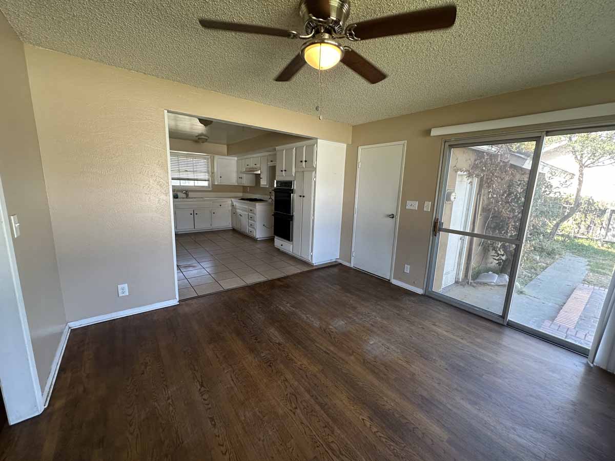 Darker toned wood flooring, a large sliding glass door leading to the backyard and another opening leading to the kitchen.