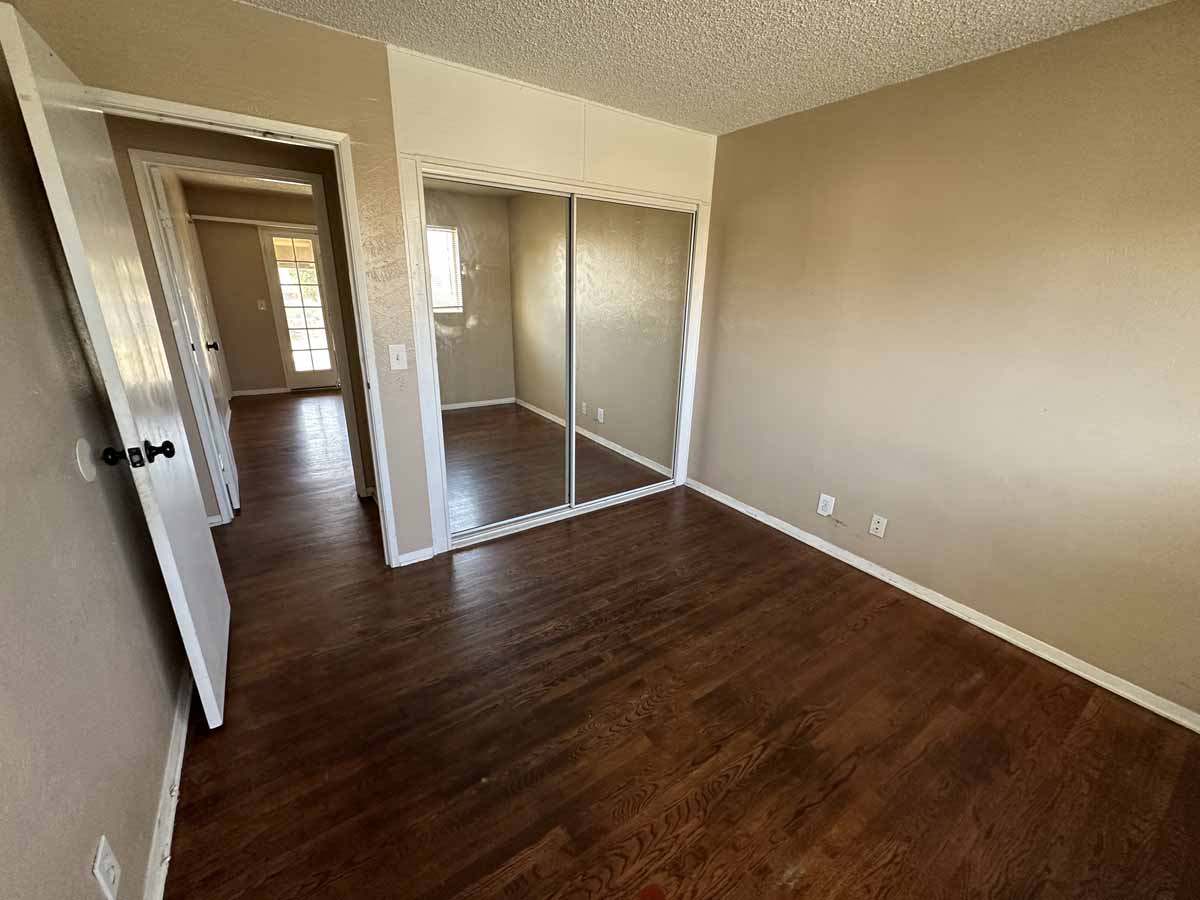 An empty bedroom with dark wood flooring, mirrored sliding closet doors, and yellow/cream colored walls.