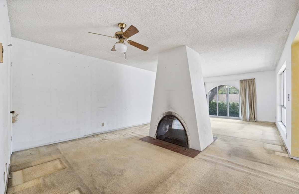 Outdated living room with beige carpet and a large fireplace in the center of the room.