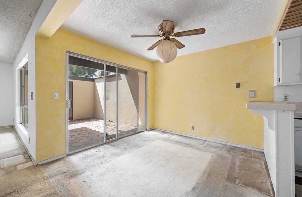 Outdated dining room with old carpet, a ceiling fan, yellow walls, and a sliding glass door leading to the patio.