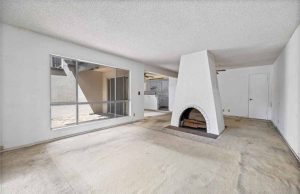 Outdated living room with beige carpet and a large fireplace in the center of the room.