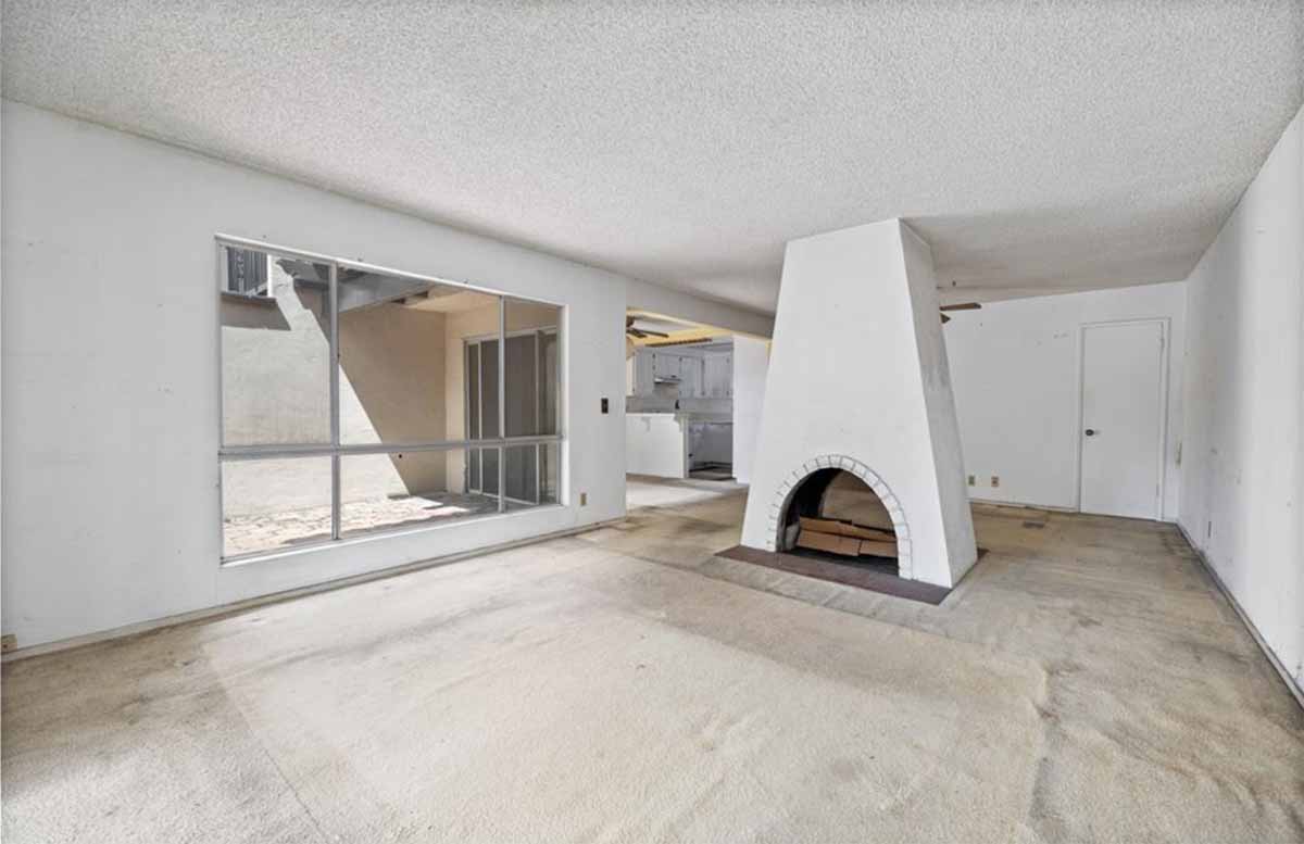 Outdated living room with beige carpet and a large fireplace in the center of the room.