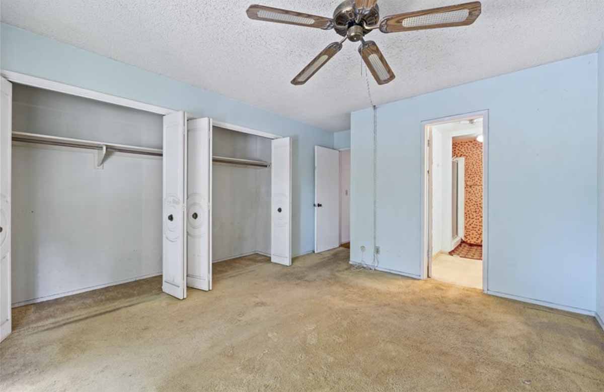 An empty bedroom with a wall of closets, a ceiling fan, door leading to bathroom.