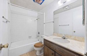 An outdated bathroom with a tub/shower combo, toilet and single sink vanity.