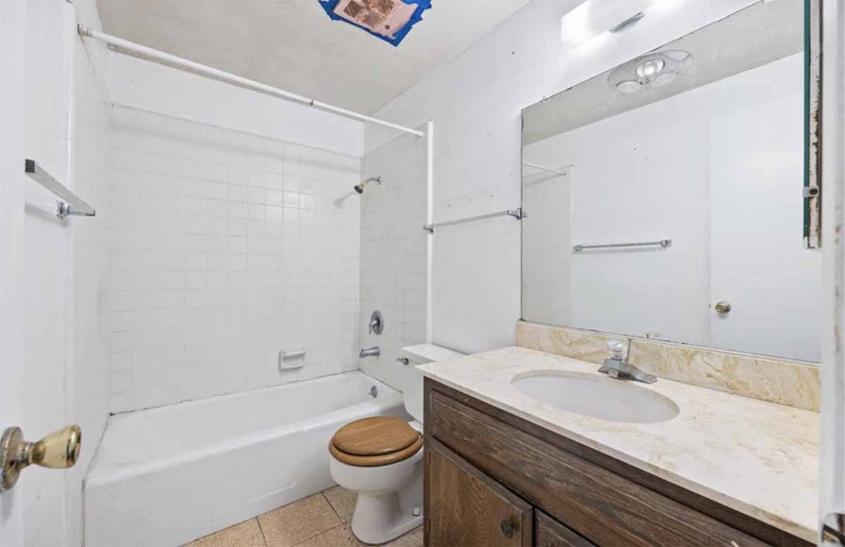 An outdated bathroom with a tub/shower combo, toilet and single sink vanity.