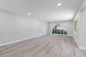 An updated living space with recessed lighting, neutral color walls and wood plank floors, and a large arched window.