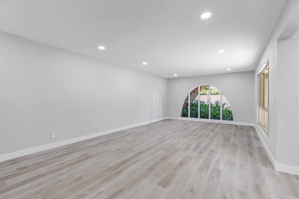 An updated living space with recessed lighting, neutral color walls and wood plank floors, and a large arched window.
