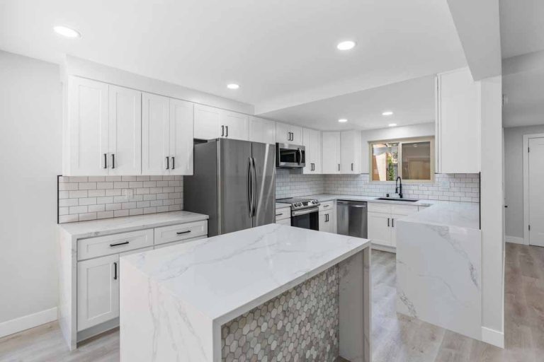 An updated kitchen with recessed lighting, neutral tones on the walls and floor, white counters and shiny stone on the island.