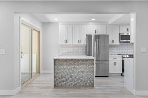An updated kitchen with recessed lighting, neutral tones on the walls and floor, white counters and shiny stone on the island.