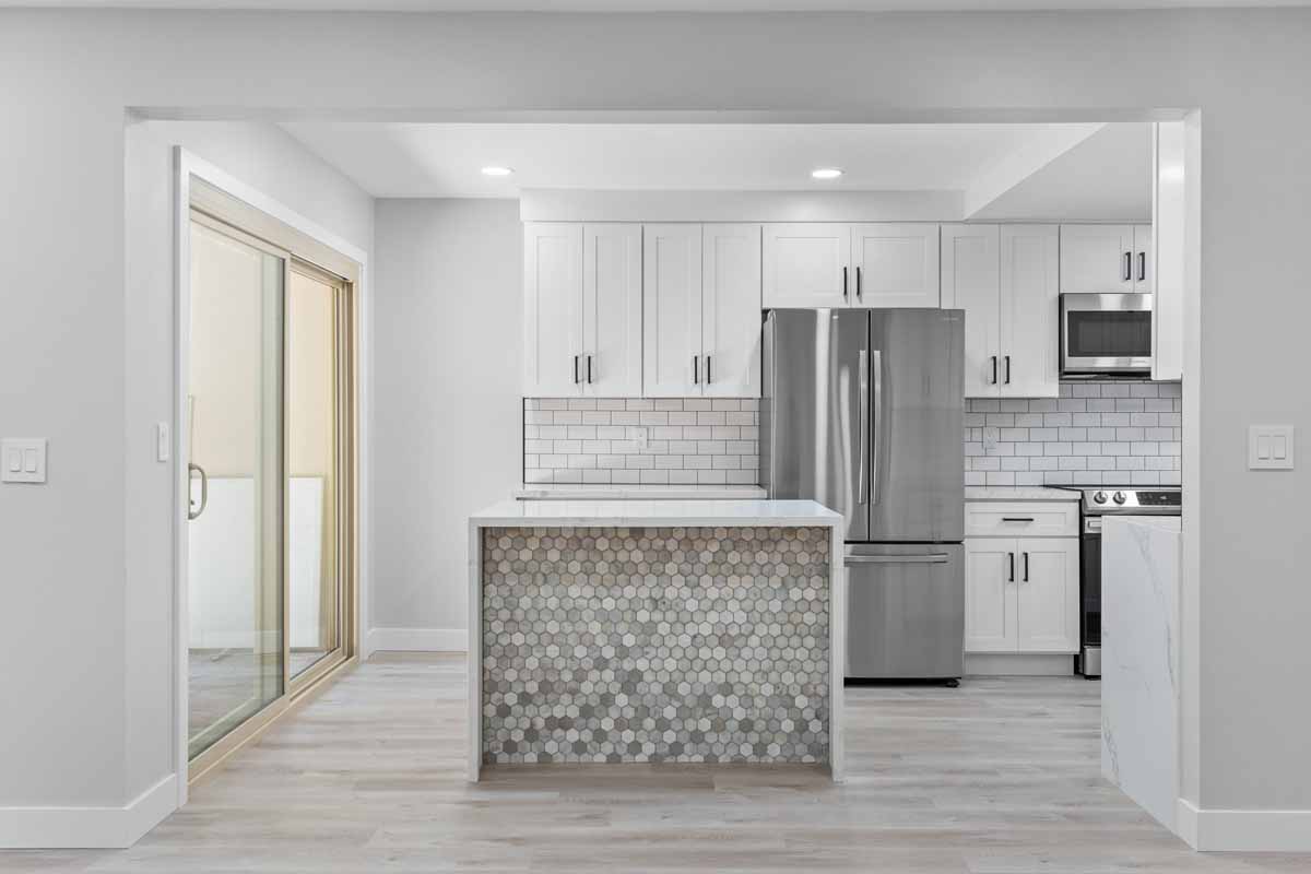 An updated kitchen with recessed lighting, neutral tones on the walls and floor, white counters and shiny stone on the island.