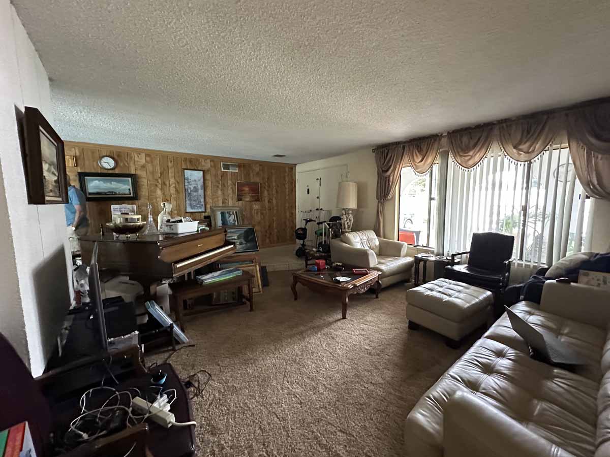 An outdated living space with couches, a piano, wood paneling on the walls, drapes and shag carpet.
