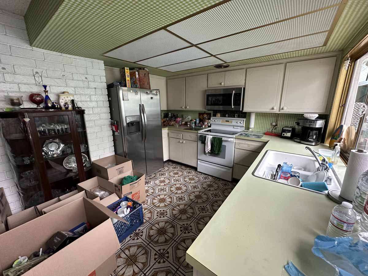 An outdated kitchen with 70s style flooring, counters and drop-ceiling. There is also an updated stainless fridge.