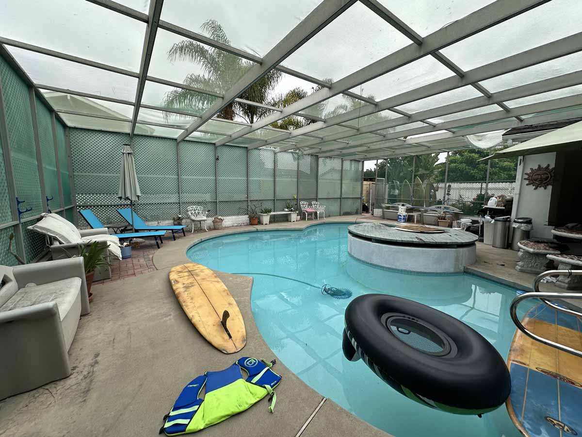A backyard enclosed pool area with surf boards, inner tubes, and lounge chairs.