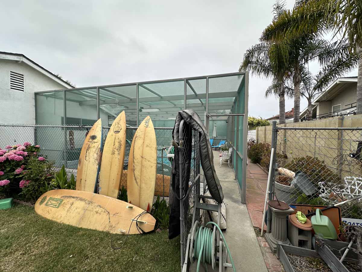 Surf boards lean up against a large outdoor pool enclosure structure.