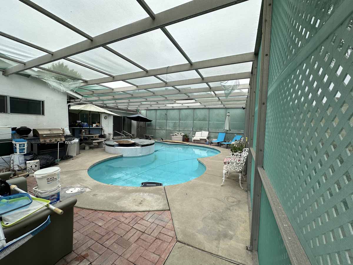 A backyard enclosed pool area with surf boards, inner tubes, and lounge chairs.
