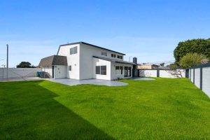 Bright green grass in a large backyard showing a two-story white home and large concrete patio.