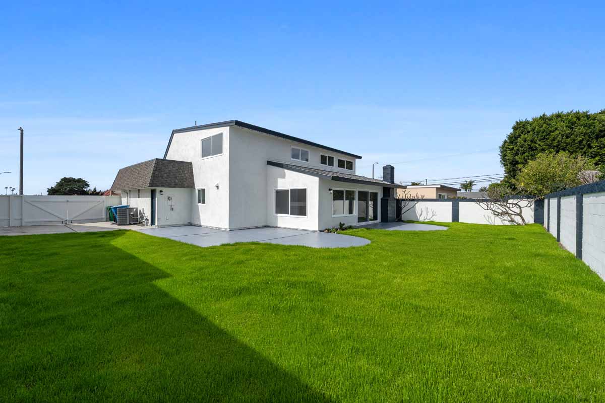Bright green grass in a large backyard showing a two-story white home and large concrete patio.