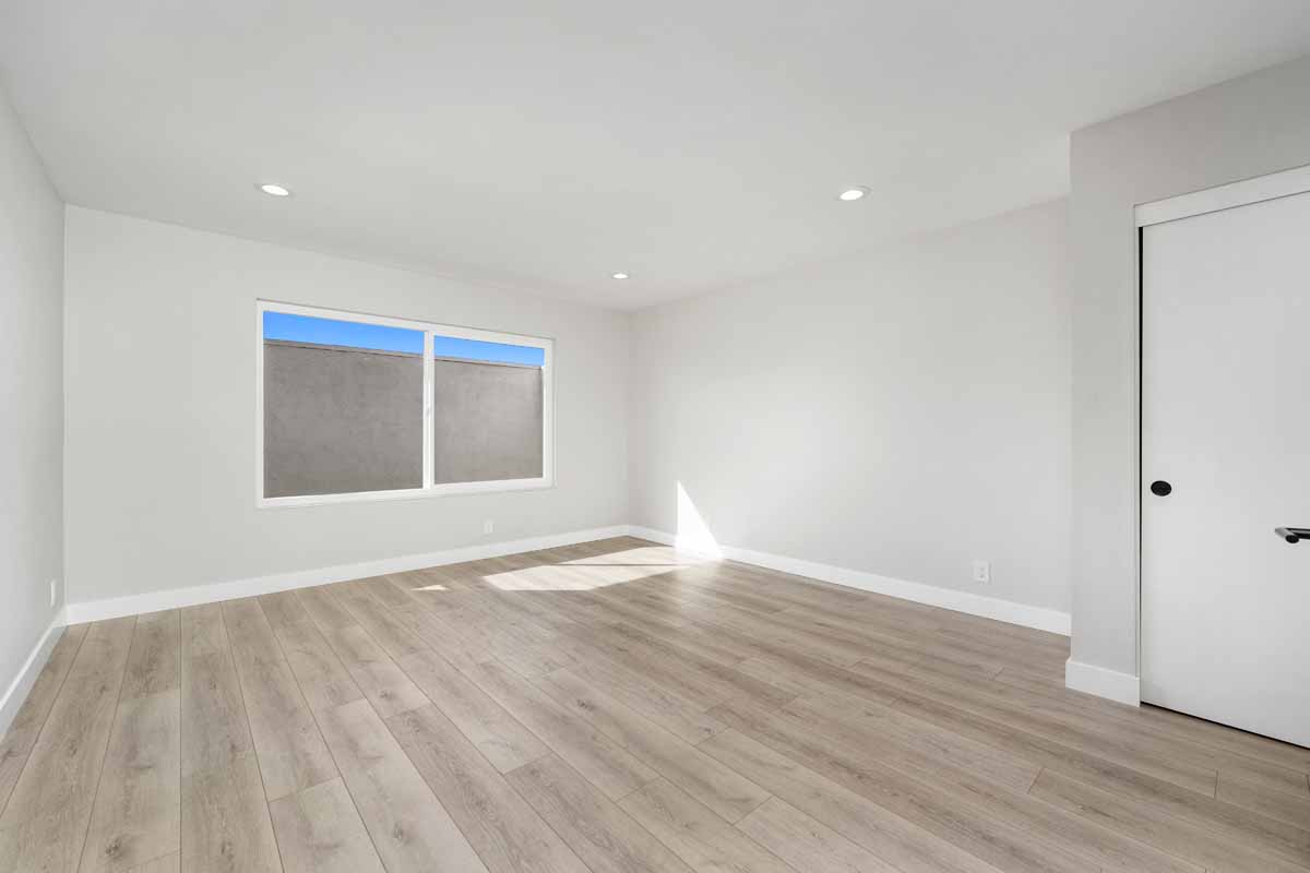An updated empty bedroom with neutral toned walls and floors, and recessed lighting.