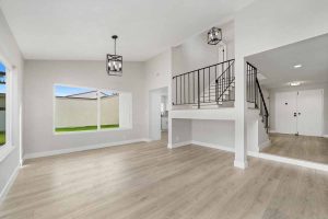 Renovated dining room with new light tone wood floors, fresh white walls, a large window and two black light fixtures.