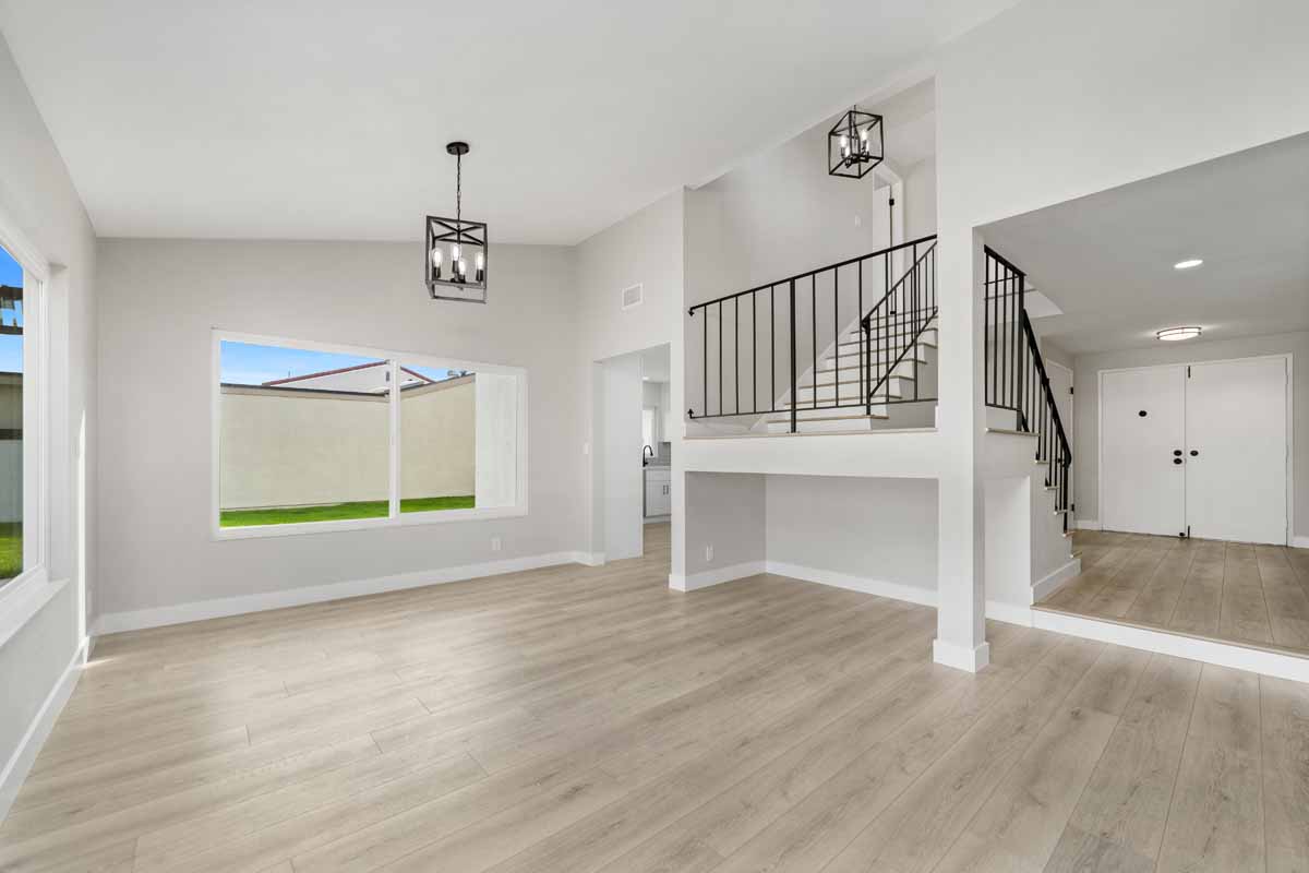 Renovated dining room with new light tone wood floors, fresh white walls, a large window and two black light fixtures.