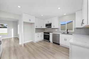 An updated kitchen with white cabinets, light stone counter tops, recessed lighting, and light neutral wall paint.