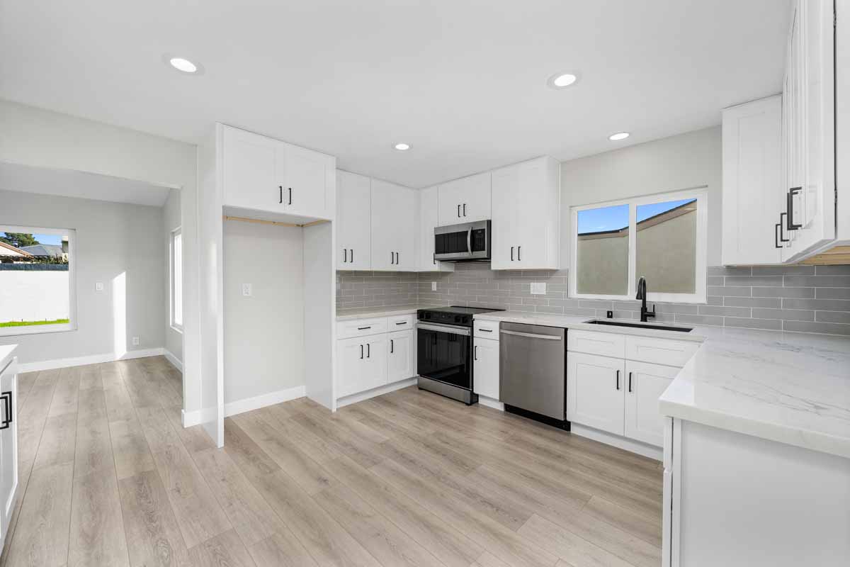 An updated kitchen with white cabinets, light stone counter tops, recessed lighting, and light neutral wall paint.
