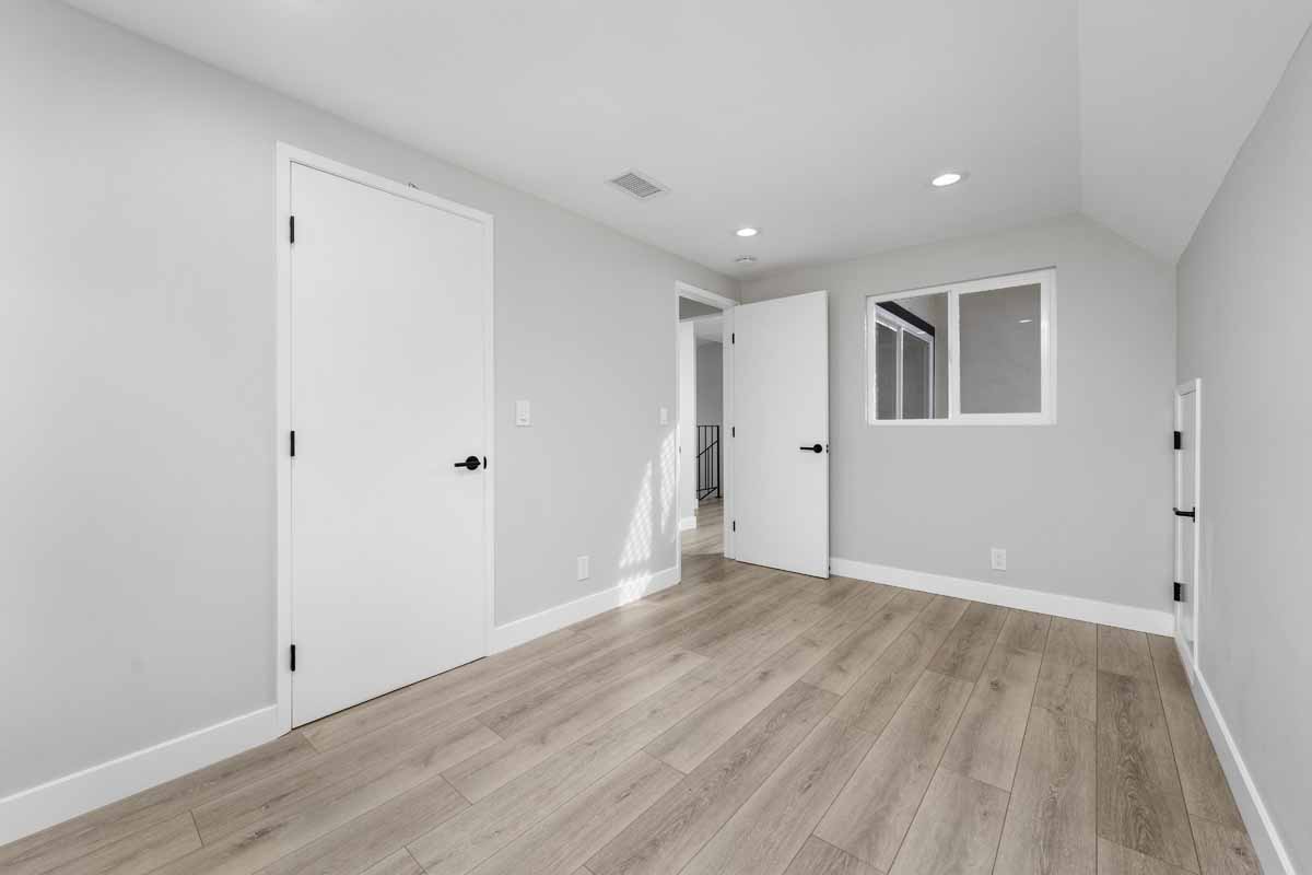 Renovated bedroom with light tone wood floors, nice neutral wall paint, recessed lighting and black handles on the doors.