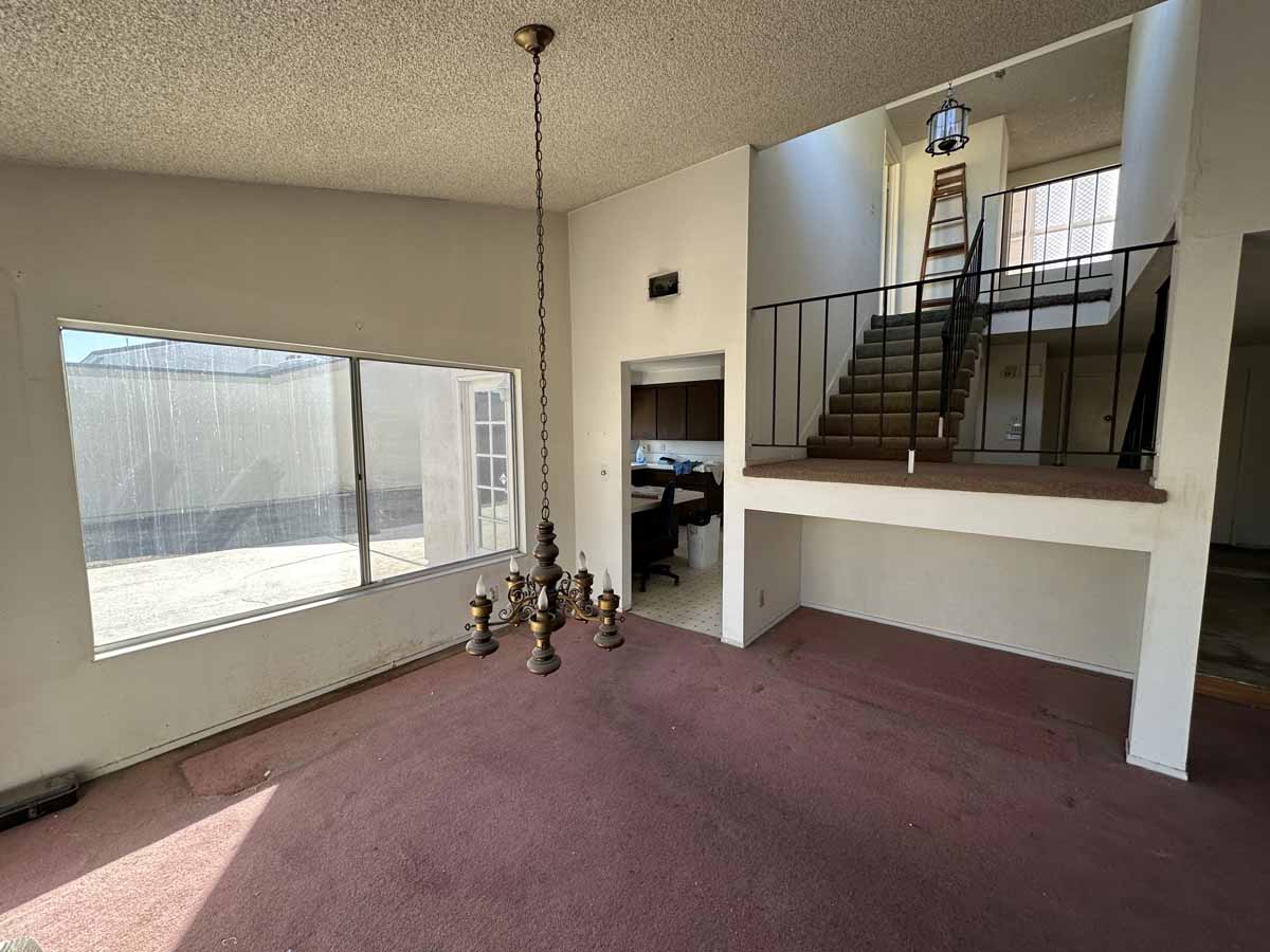Outdated living space pre-reno showing purple carpet, white walls and popcorn ceilings.