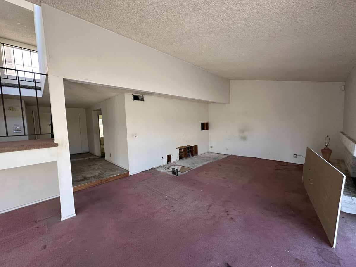 Outdated living space pre-reno showing purple carpet, white walls and popcorn ceilings.