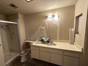 Outdated bathroom with step-in shower, toilet with wooden seat and single sink vanity.