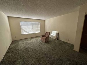 Outdated living space with old beige carpet and popcorn ceilings.