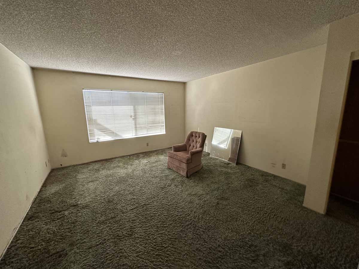 Outdated living space with old beige carpet and popcorn ceilings.