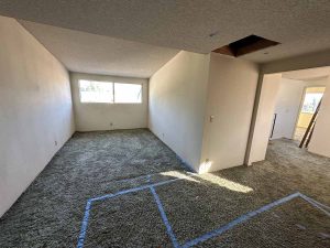 Outdated living space with old beige carpet and popcorn ceilings.