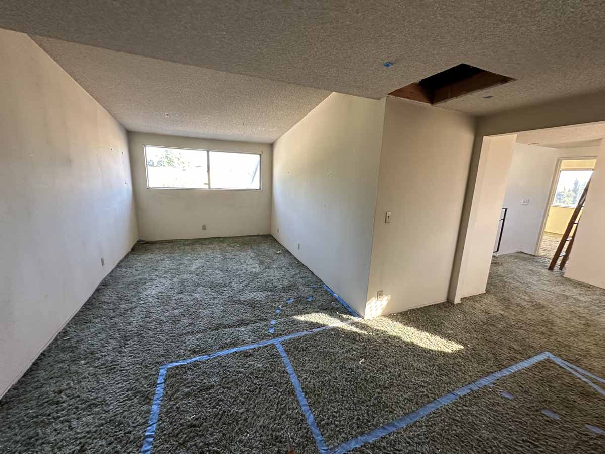 Outdated living space with old beige carpet and popcorn ceilings.