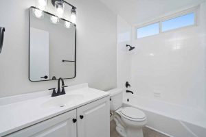 An updated bathroom with a one sink white vanity with black fixtures, toilet, and a tub/shower combo.