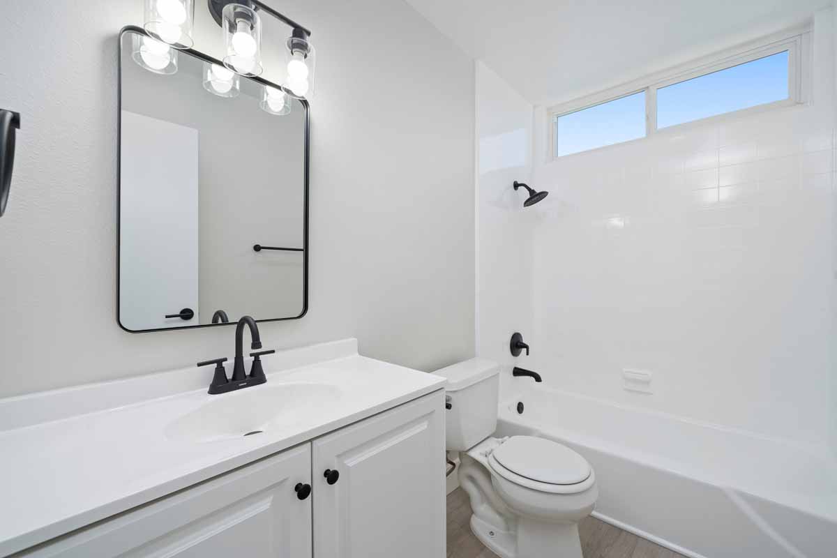 An updated bathroom with a one sink white vanity with black fixtures, toilet, and a tub/shower combo.