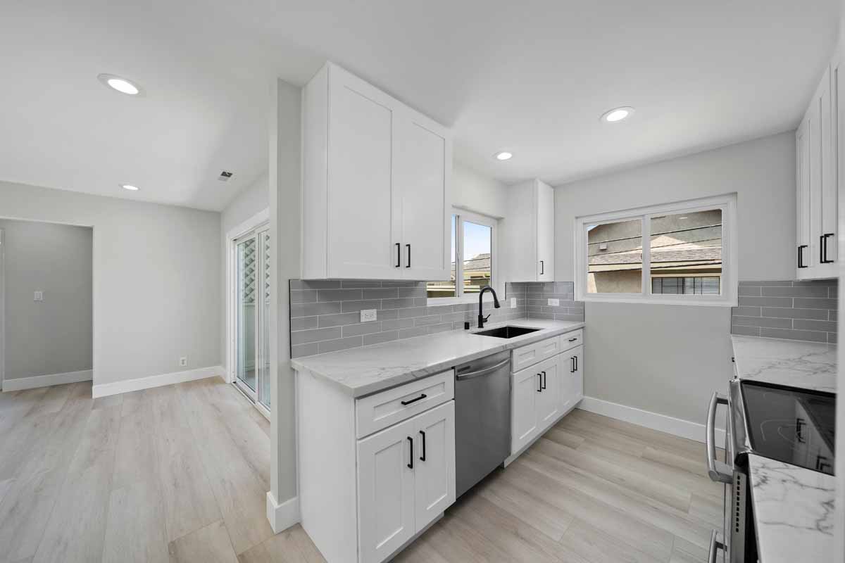 An updated kitchen with white cabinets, light stone counter tops, recessed lighting, and light neutral wall paint.