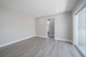 An empty living space with fresh light neutral paint on the walls, recessed lighting, new light wood flooring and a sliding glass door.