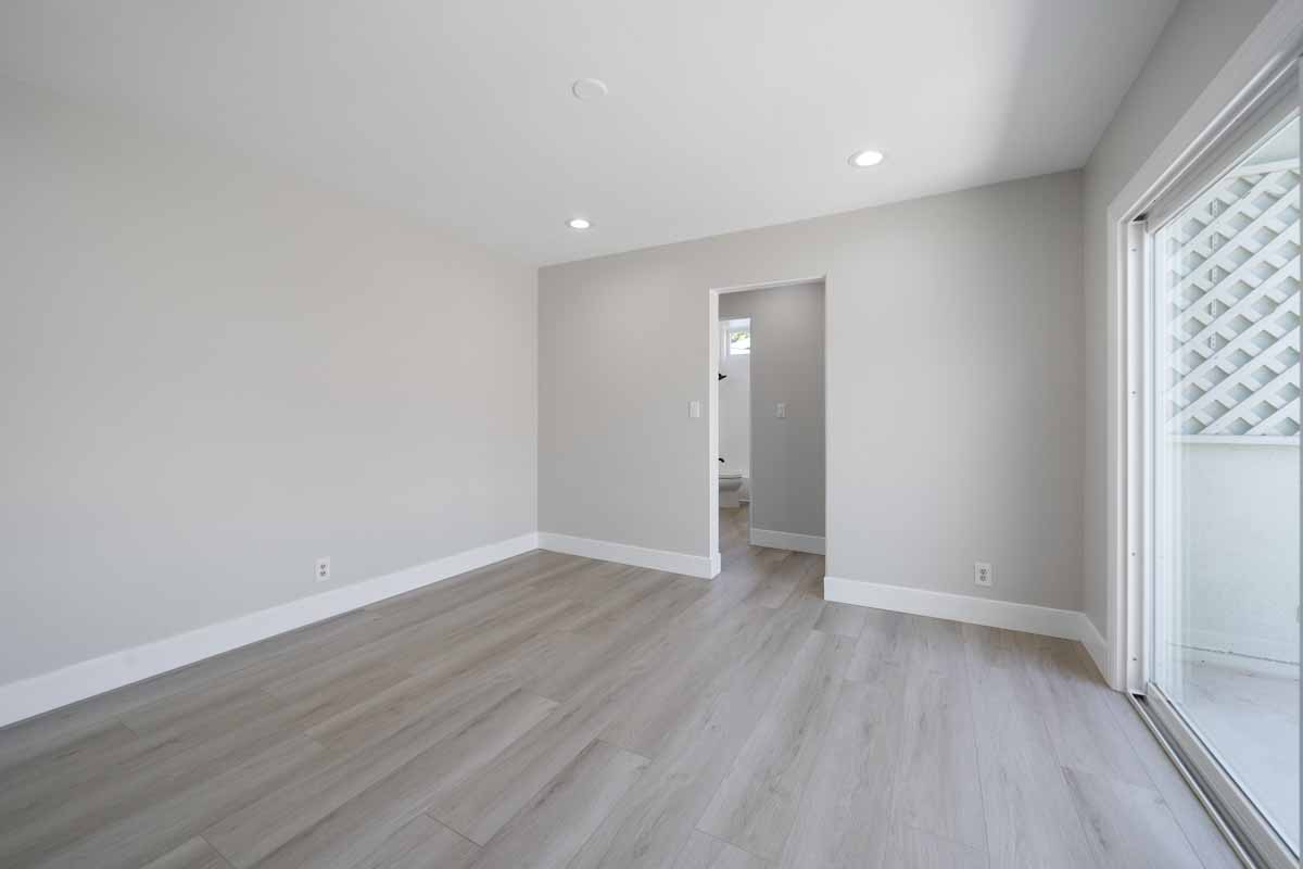 An empty living space with fresh light neutral paint on the walls, recessed lighting, new light wood flooring and a sliding glass door.