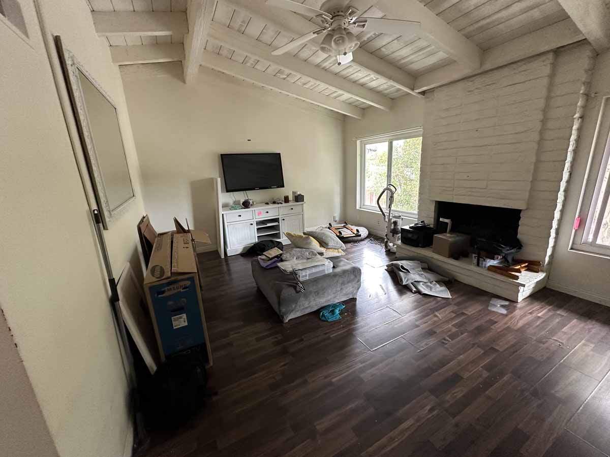 A living room with dark wood flooring, a couch and a tv on a stand. The walls and ceiling have light neutral paint.