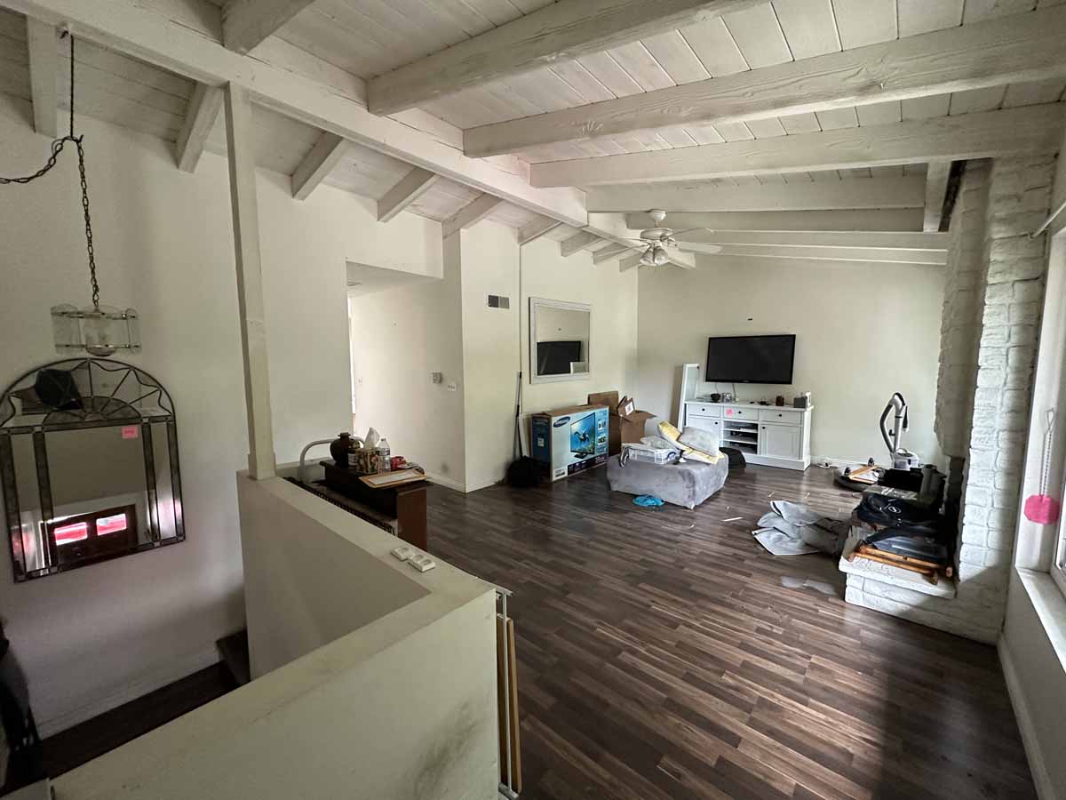 A living room with dark wood flooring, a couch and a tv on a stand. The walls and ceiling have light neutral paint.