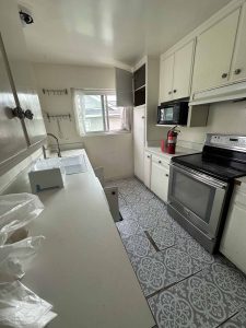An outdated galley style kitchen with light painted cabinets and light colored counter tops.