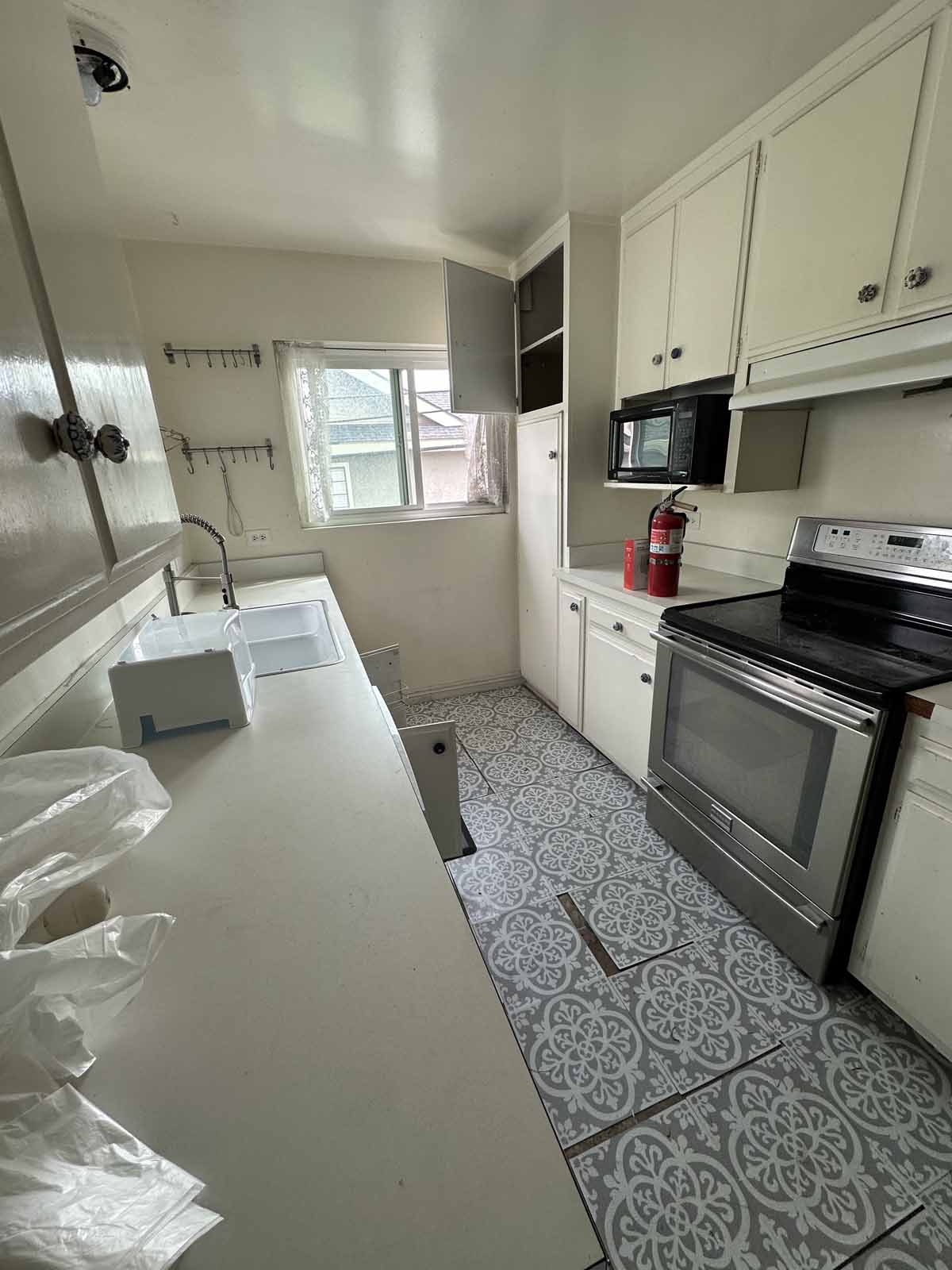 An outdated galley style kitchen with light painted cabinets and light colored counter tops.