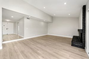 An empty living space with light wood flooring and a black fireplace. The ceiling has recessed lighting.