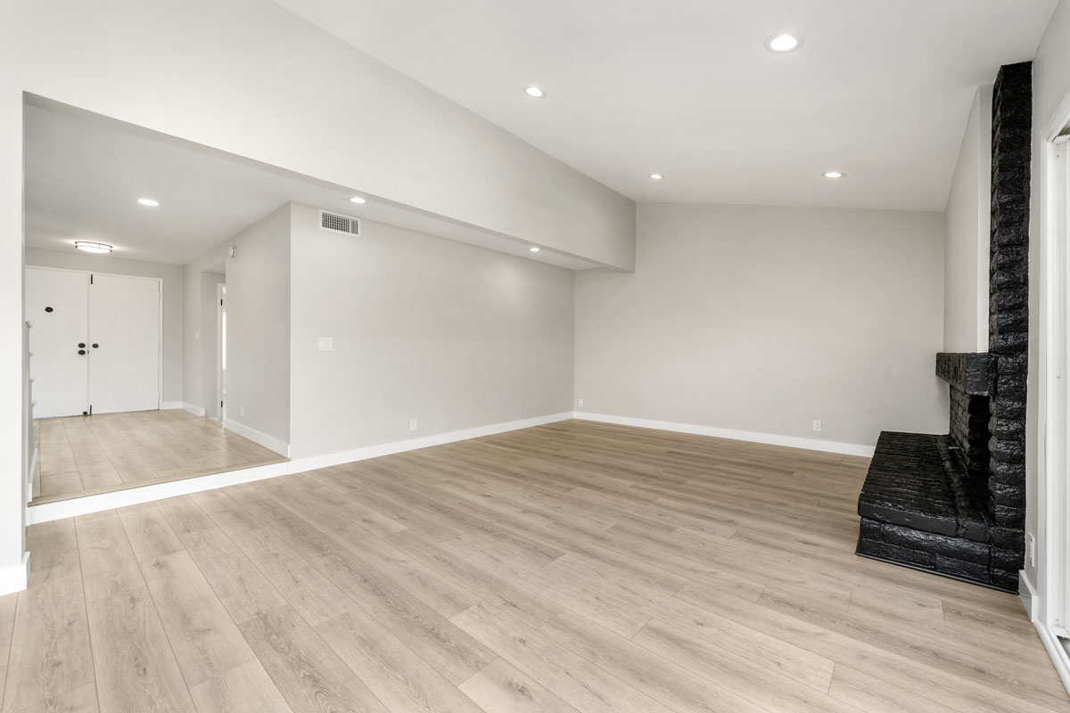 An empty living space with light wood flooring and a black fireplace. The ceiling has recessed lighting.