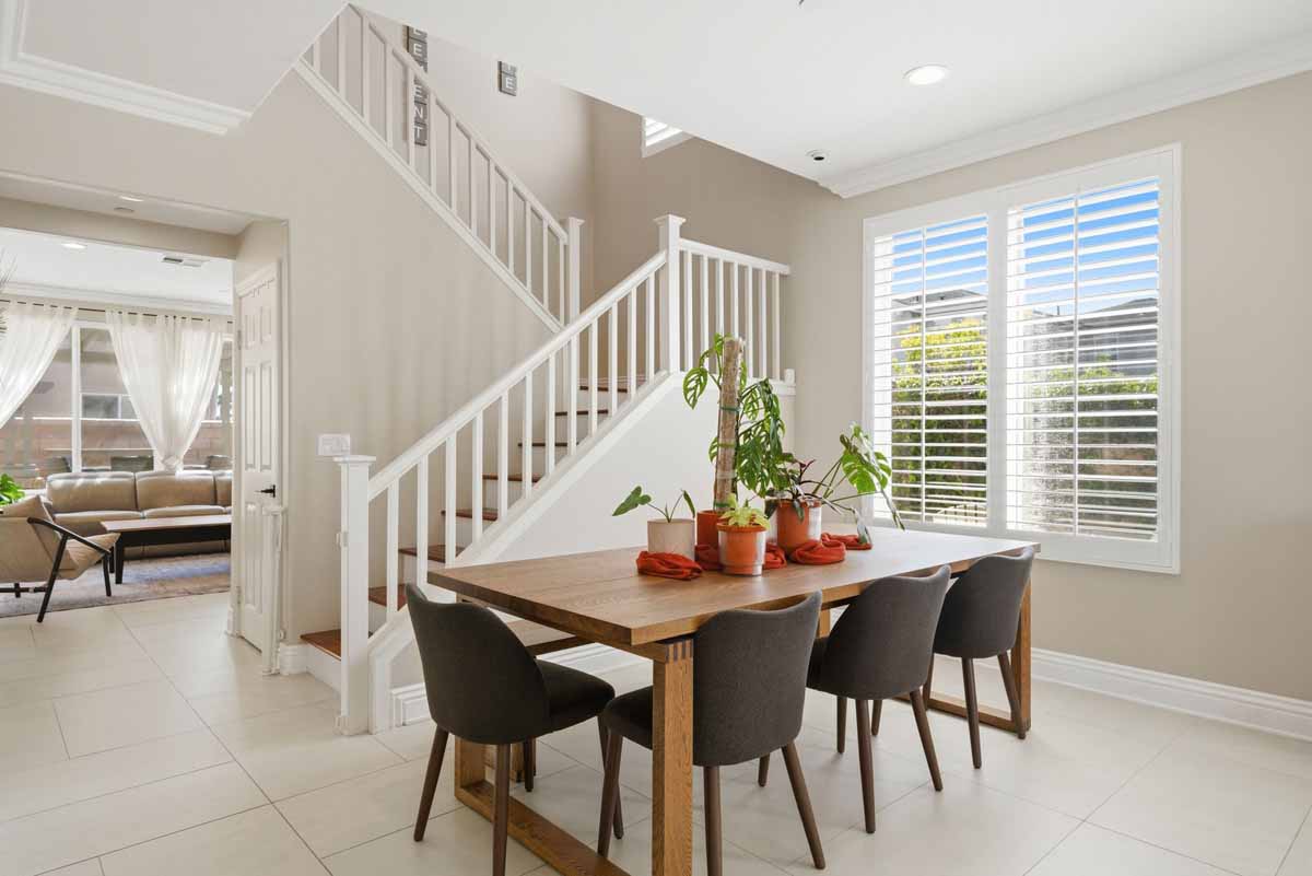 Dining table with chairs on tiled floors with stairs leading up in the background.