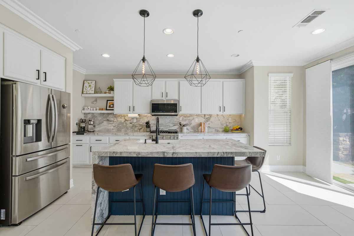 Updated kitchen with navy blue painted island cabinet and white upper cabinets all with white stone counter tops.